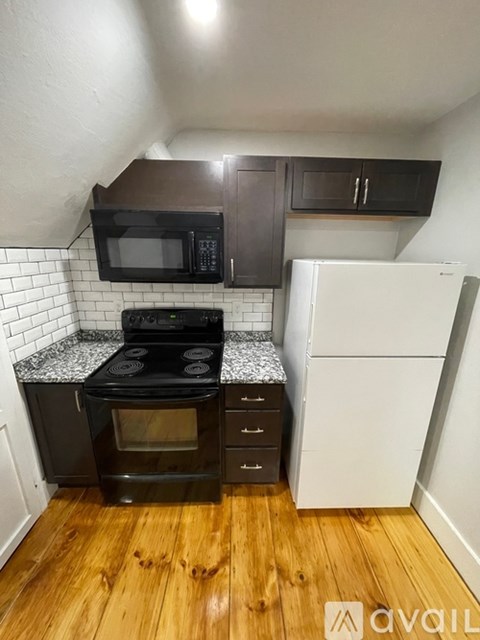 A kitchen with a black oven and microwave, a white fridge, and wooden floors.