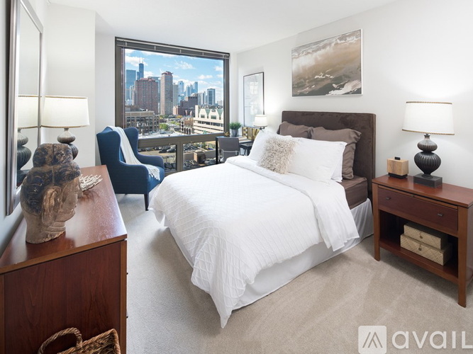 A bedroom with a large bed, a blue chair, and a city view through the window.