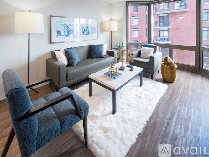 A living room with a grey couch, a blue chair, a white rug, and a wooden floor.