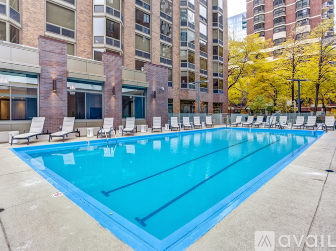 A large swimming pool with lounge chairs and apartment buildings in the background.