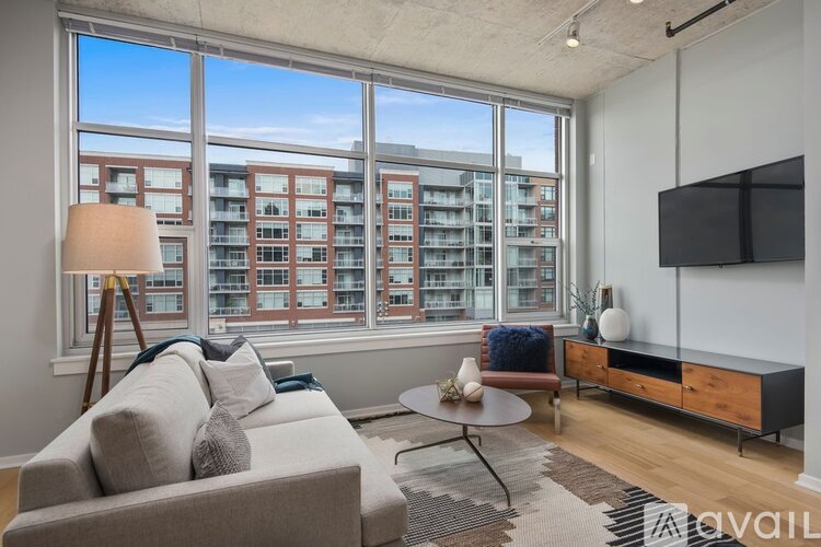 A living room with a grey couch, a round table, a wooden cabinet, and a large window overlooking a building.