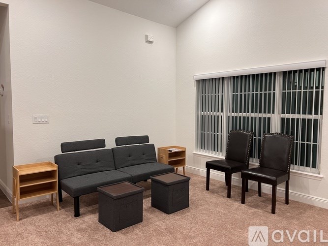 A living room with a grey couch, two black chairs, and a small wooden table.
