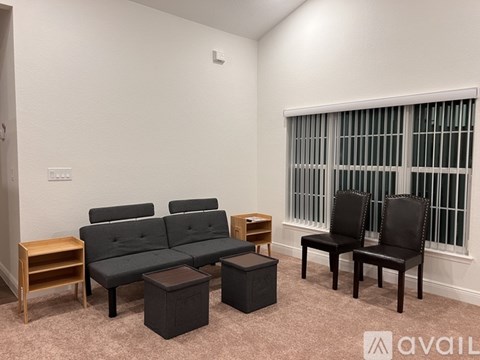 A living room with a grey couch, two black chairs, and a small wooden table.