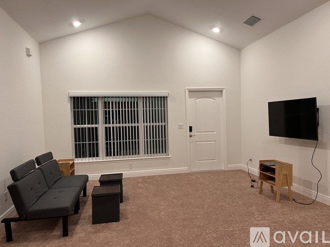 A living room with a black sofa, a small table, and a flat screen TV mounted on the wall.