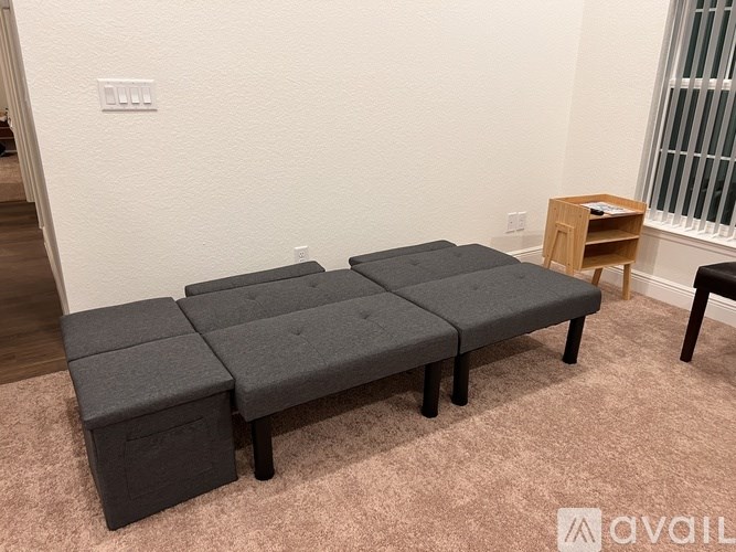 A grey ottoman with storage box and a small wooden table with a book on it.