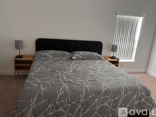 A bed with a grey and white patterned comforter sits in a room with a wooden nightstand and lamp beside it.