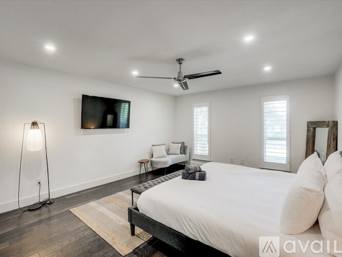 A bedroom with a bed, a fan, and a painting on the wall.