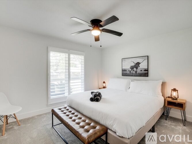 A bedroom with a large bed, a ceiling fan, and a painting on the wall.