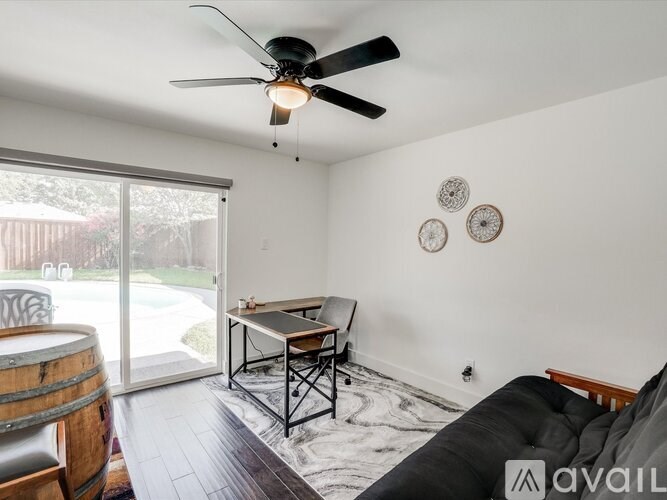A living room with a black couch, a wooden table, a ceiling fan, and a sliding glass door.