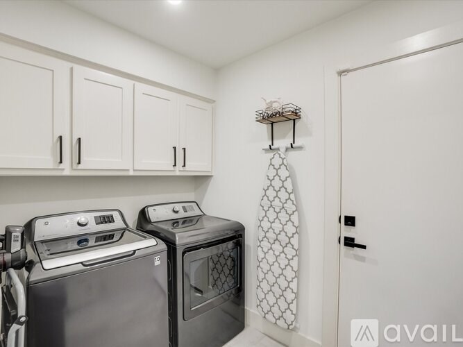 A small laundry room with a washer and dryer and a white ironing board.