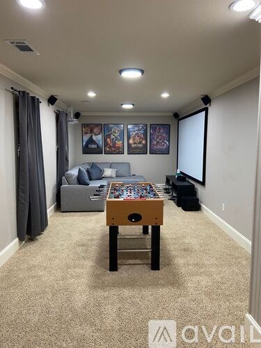 A room with a foosball table in the center and a couch in the background.