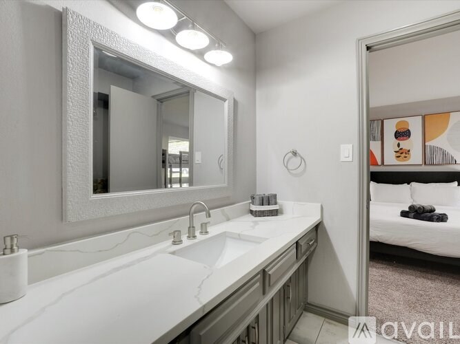 A bathroom with a sink, mirror, and a bedroom in the background.