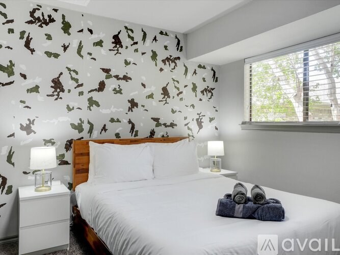 A bedroom with a bed, nightstands, and a leafy wallpaper.