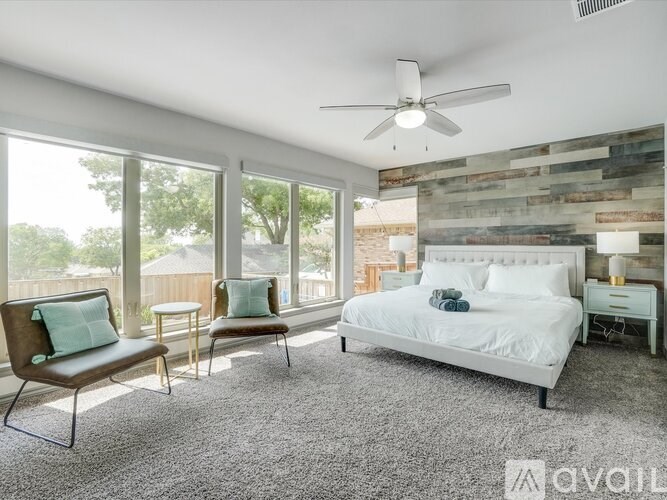 A bedroom with a bed, two chairs, and a ceiling fan.
