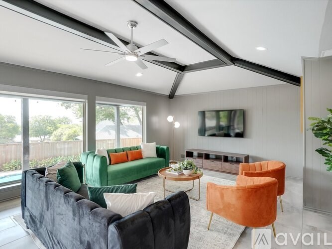 A living room with a black couch, green couch, orange chair, and a ceiling fan.