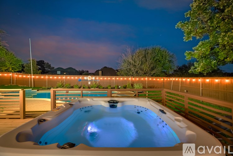 A hot tub is lit up at night with lights on the fence.