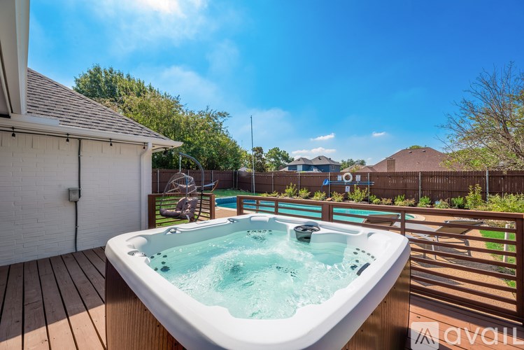 A hot tub is on a deck with a house and trees in the background.
