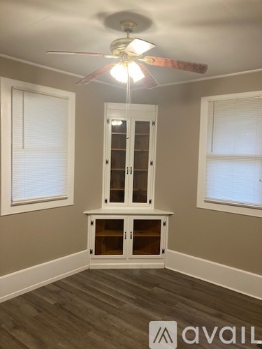A room with a ceiling fan and a cabinet under a window.