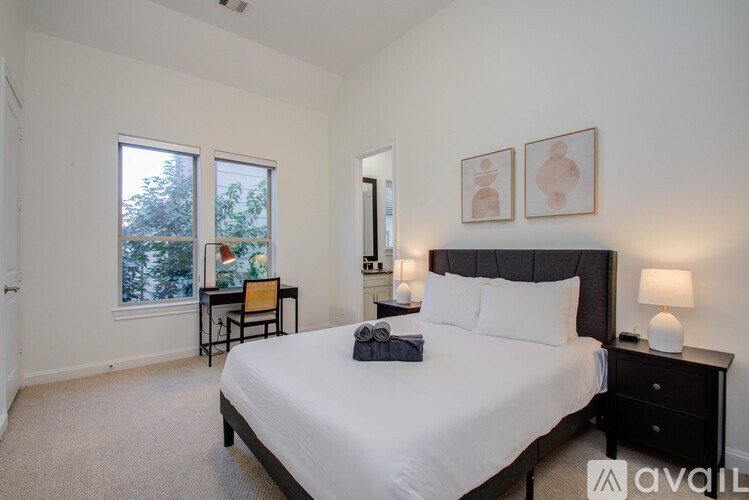 A bedroom with a large bed, a desk with a chair, and two framed pictures on the wall.