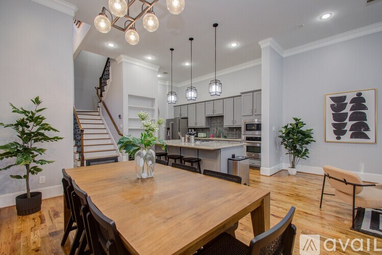 A dining room with a wooden table and chairs, a staircase, and a kitchen area in the background.
