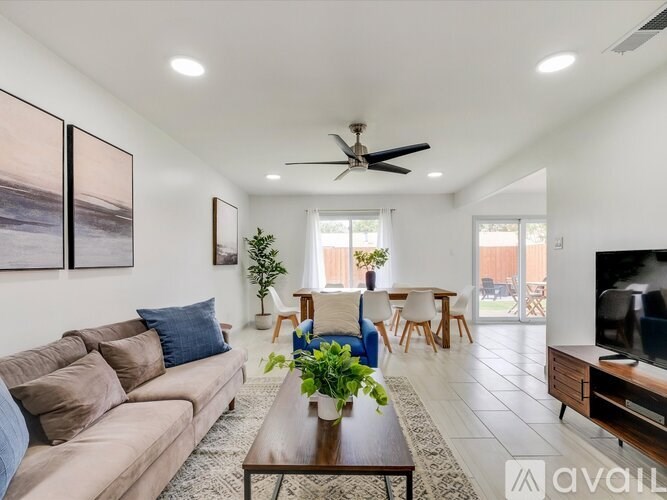 A living room with a couch, a coffee table, a ceiling fan, and a television.