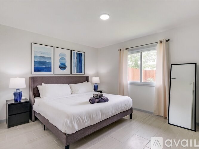 A bedroom with a large bed, two lamps, and a painting on the wall.