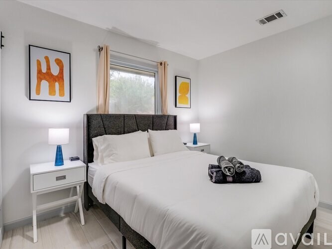 A bedroom with a large bed, a nightstand with a blue lamp, and two wall art pieces.