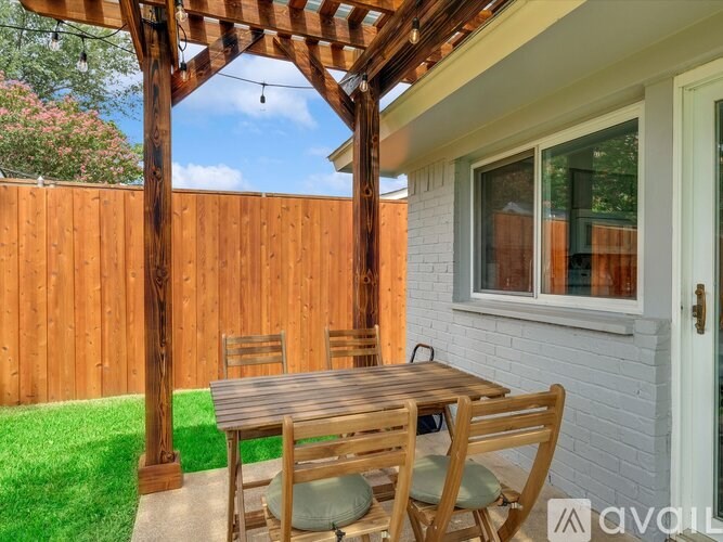 A wooden table and chairs are set up under a pergola in a backyard.