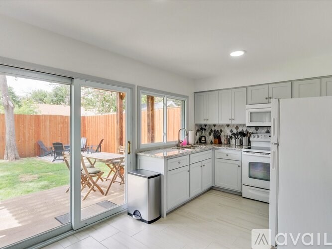 A kitchen with white cabinets and appliances, a dining table with chairs, and a sliding glass door leading to a backyard.