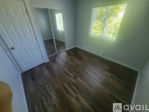 A room with wooden flooring and a window letting in sunlight.