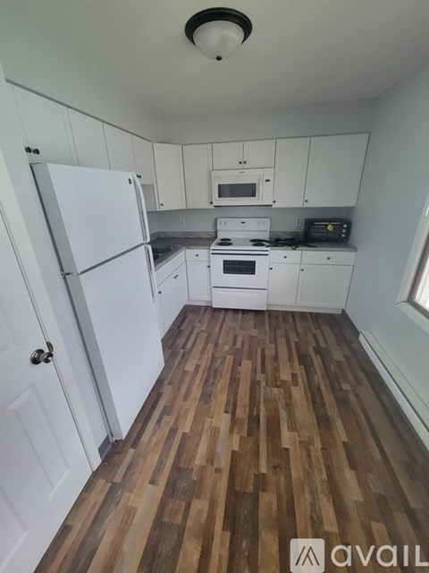 A kitchen with white appliances and wooden floors.