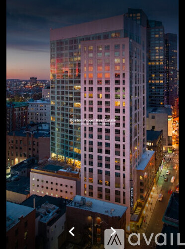 A tall building with many windows is lit up at dusk.