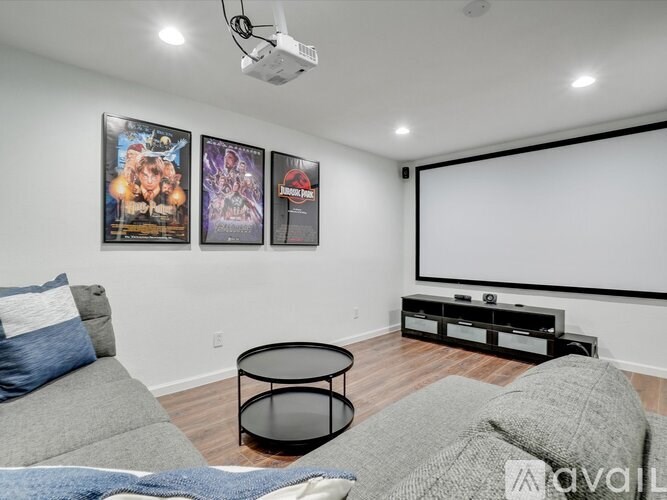 A living room with a grey couch, a black coffee table, and a wall with three posters.