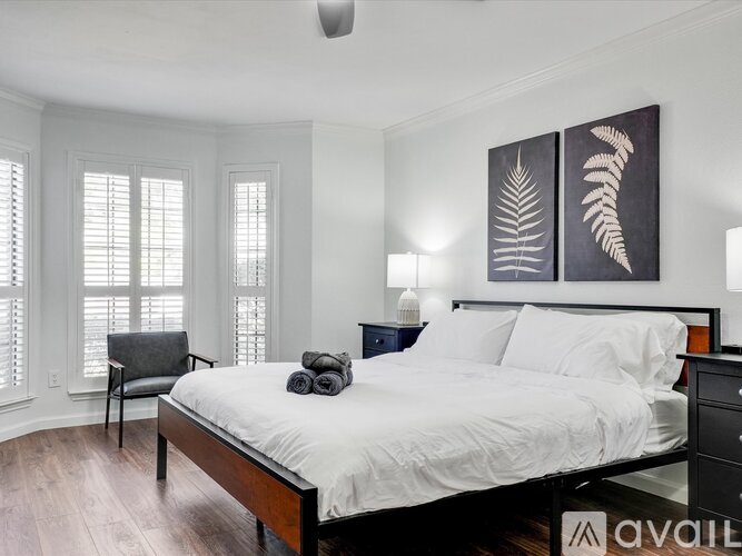 A bedroom with a bed, chair, and two paintings on the wall.