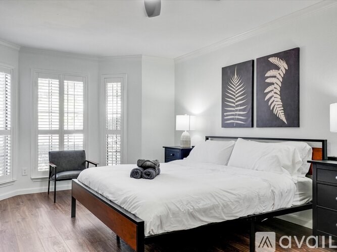 A bedroom with a bed, chair, and two paintings on the wall.