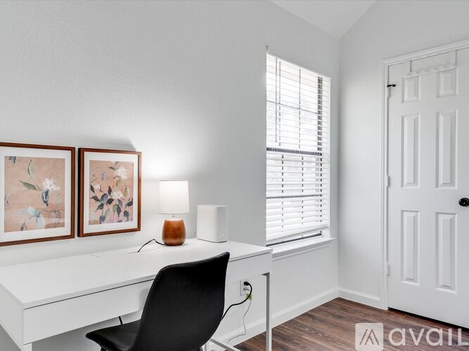 A white desk with a black chair and two framed pictures on the wall.