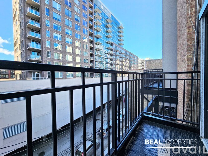 A balcony with a black railing overlooks a parking lot and a tall building.