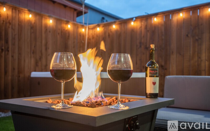Two glasses of wine and a bottle are on a table with a fire in the middle.