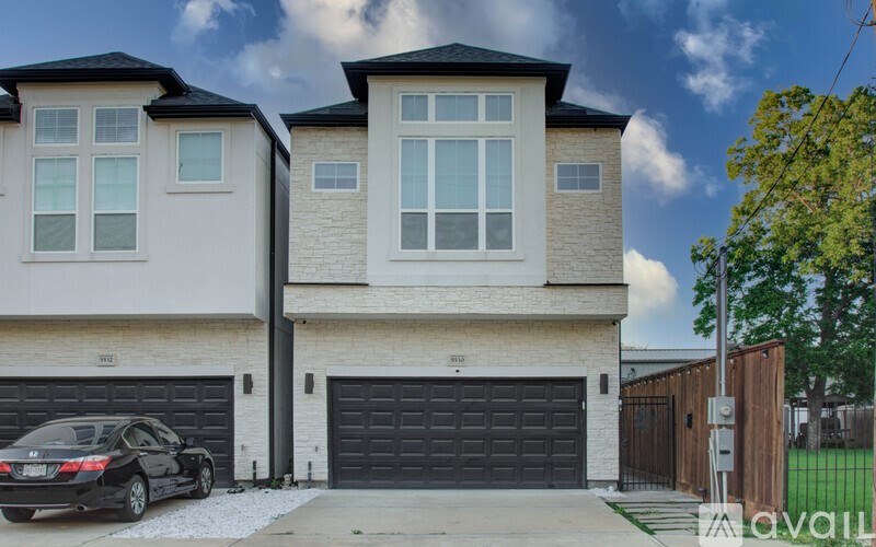A black car is parked in front of a two-story house with a garage.