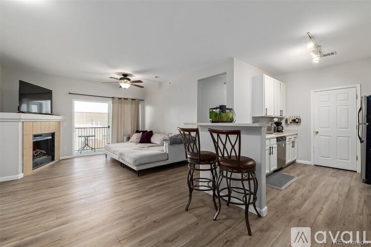 A well-lit, spacious living room with a fireplace and a kitchen area with white cabinets.