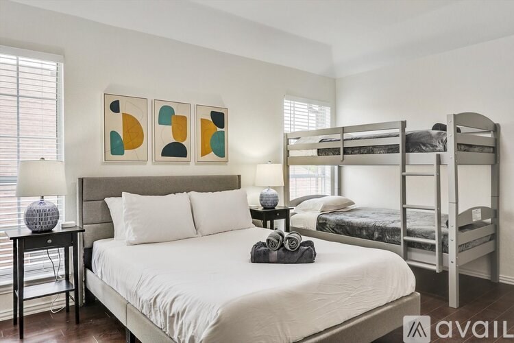 A bedroom with a white bed, a grey headboard, and a bunk bed in the background.