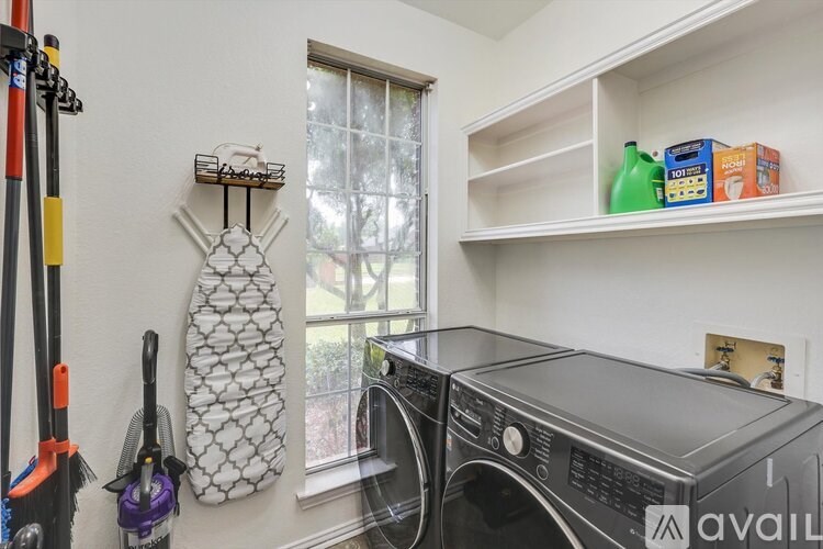 A laundry room with a washer and dryer, a mop, a broom, and a detergent bottle.