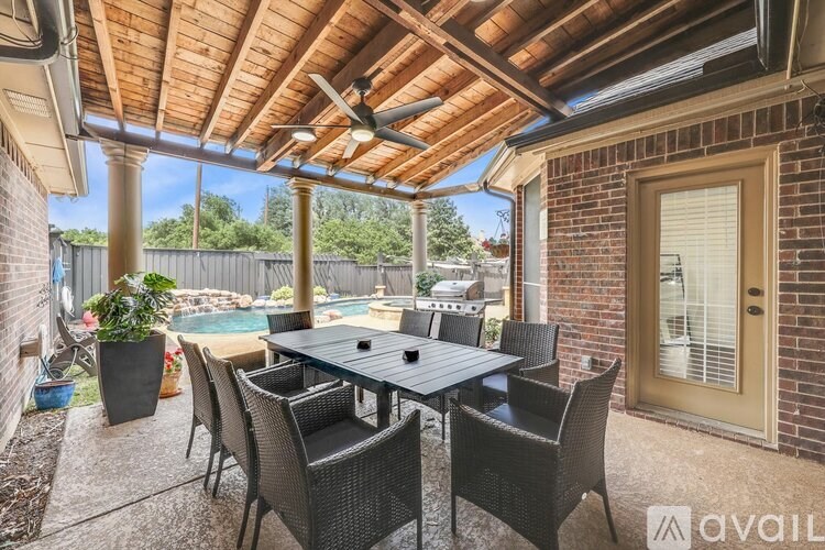 A patio with a table and chairs is covered by a wooden roof.