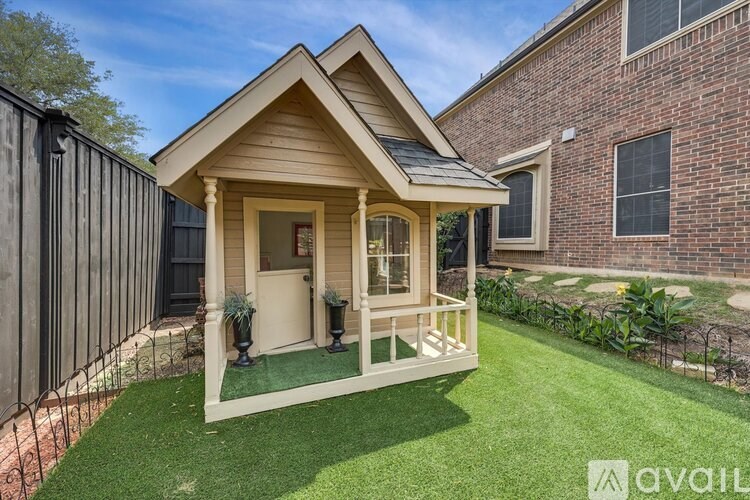 A small wooden cabin with a porch is situated in a grassy yard.