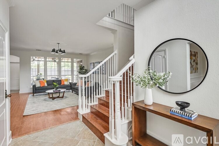 A living room with a staircase and a mirror on the wall.