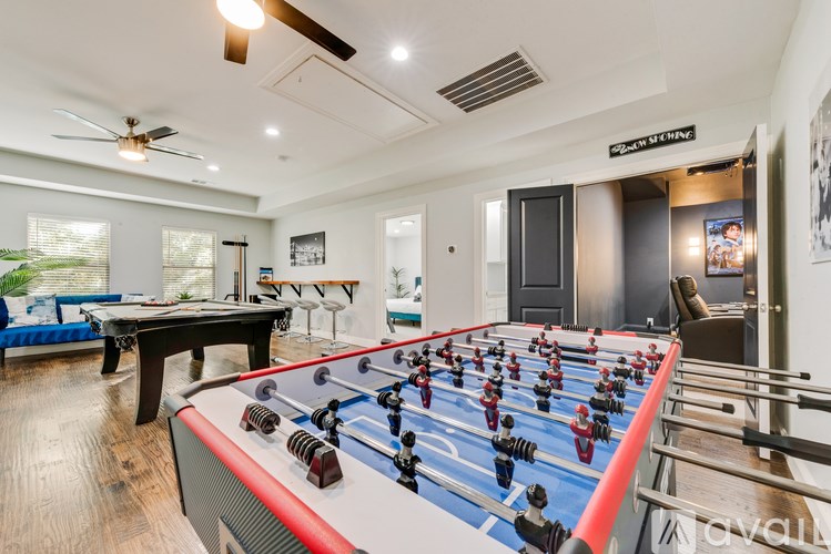 A foosball table is in the middle of a room with a pool table and a couch.
