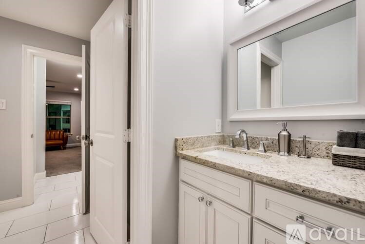 A bathroom with a sink, mirror, and a door leading to a living room.