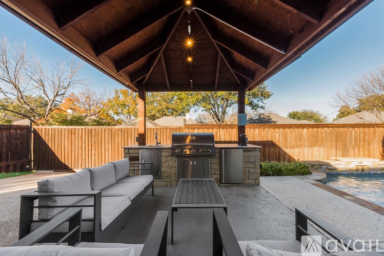 A covered outdoor seating area with a fireplace and a pool in the background.