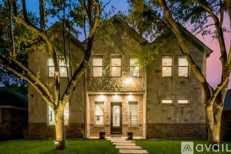 A house with a front yard and trees is lit up at night.