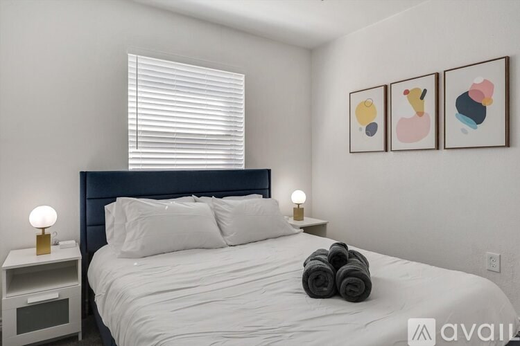 A bed with a white comforter and two rolled towels on top.